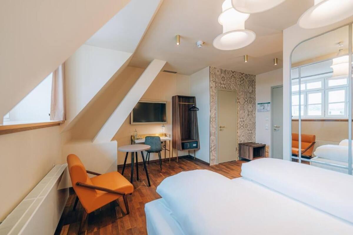 Una habitación de hotel moderna con zona de dormir en altura, un escritorio con silla, televisor y un espejo grande.