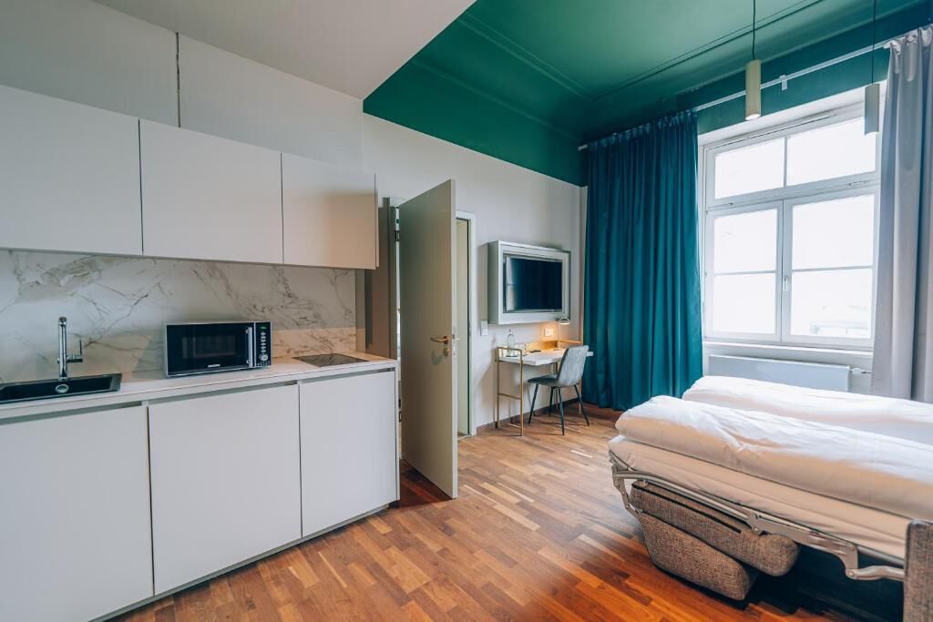 A compact room with a kitchenette, a bed, a desk with a chair, and a TV.