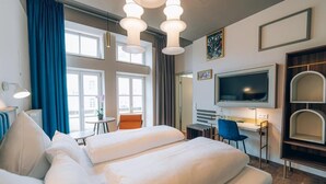 A hotel room with a bed, a desk, a chair, a TV, and a window with curtains. - Hotel Amalia - Boutique Hotel (Landshut)