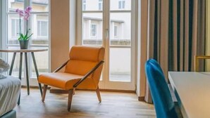 A modern living room with a large window, a blue chair, an orange chair, and a small table with a plant. - Hotel Amalia - Boutique Hotel (Landshut)