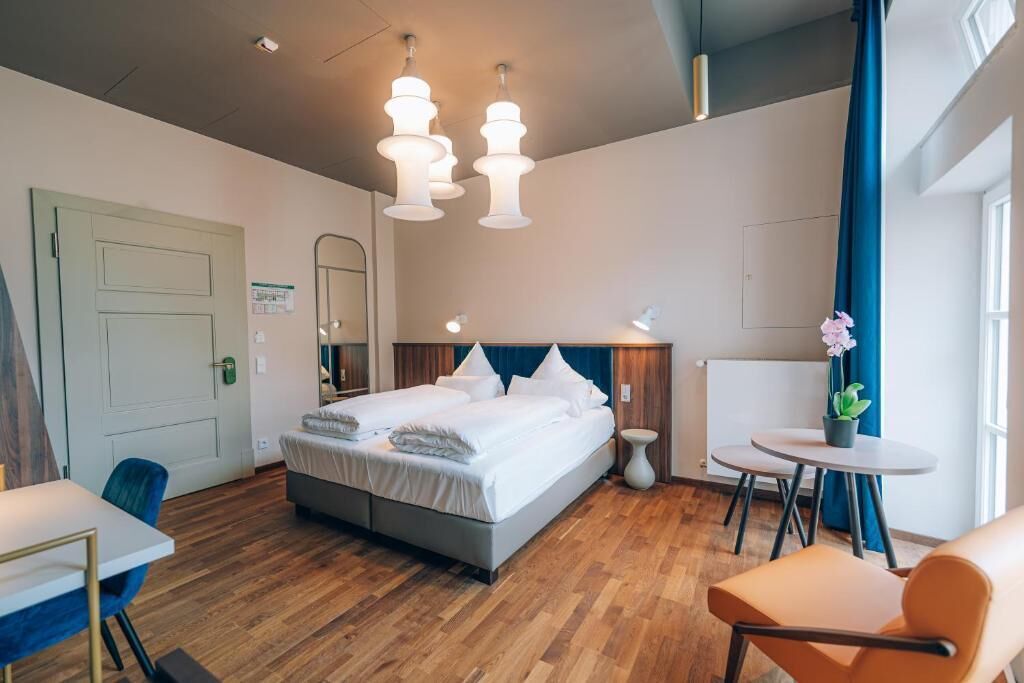 A modern hotel room with a large bed, bedside tables, a round table, and a chair.