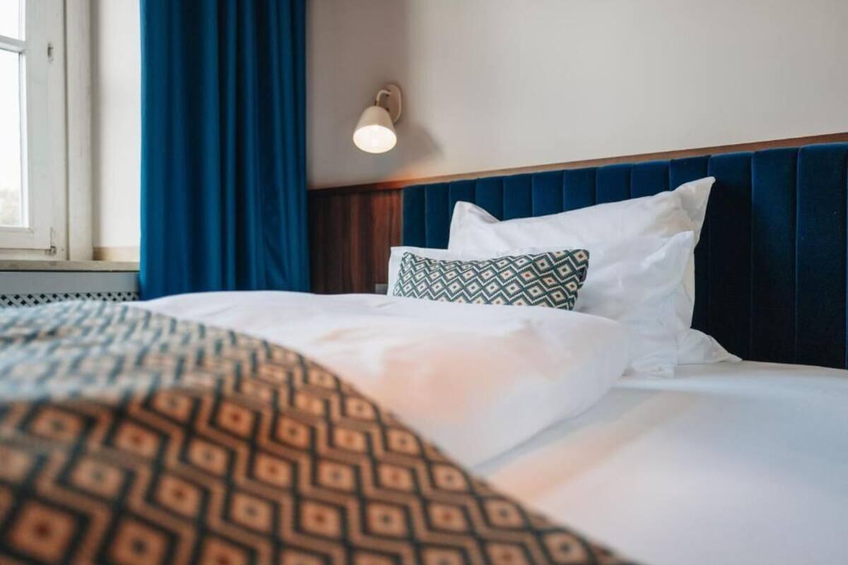 Una cama bien hecha con ropa de cama estampada, un cabecero azul y una lámpara fijada a la pared.