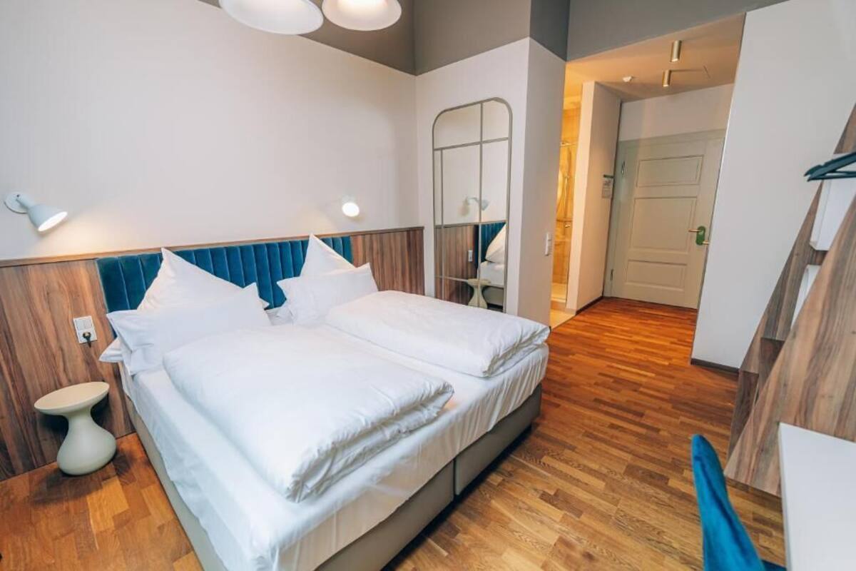 Una cama doble con sábanas blancas, cabecera de madera y mesita de noche.