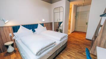 Un lit double avec du linge de lit blanc, une tête de lit en bois et une table de chevet.