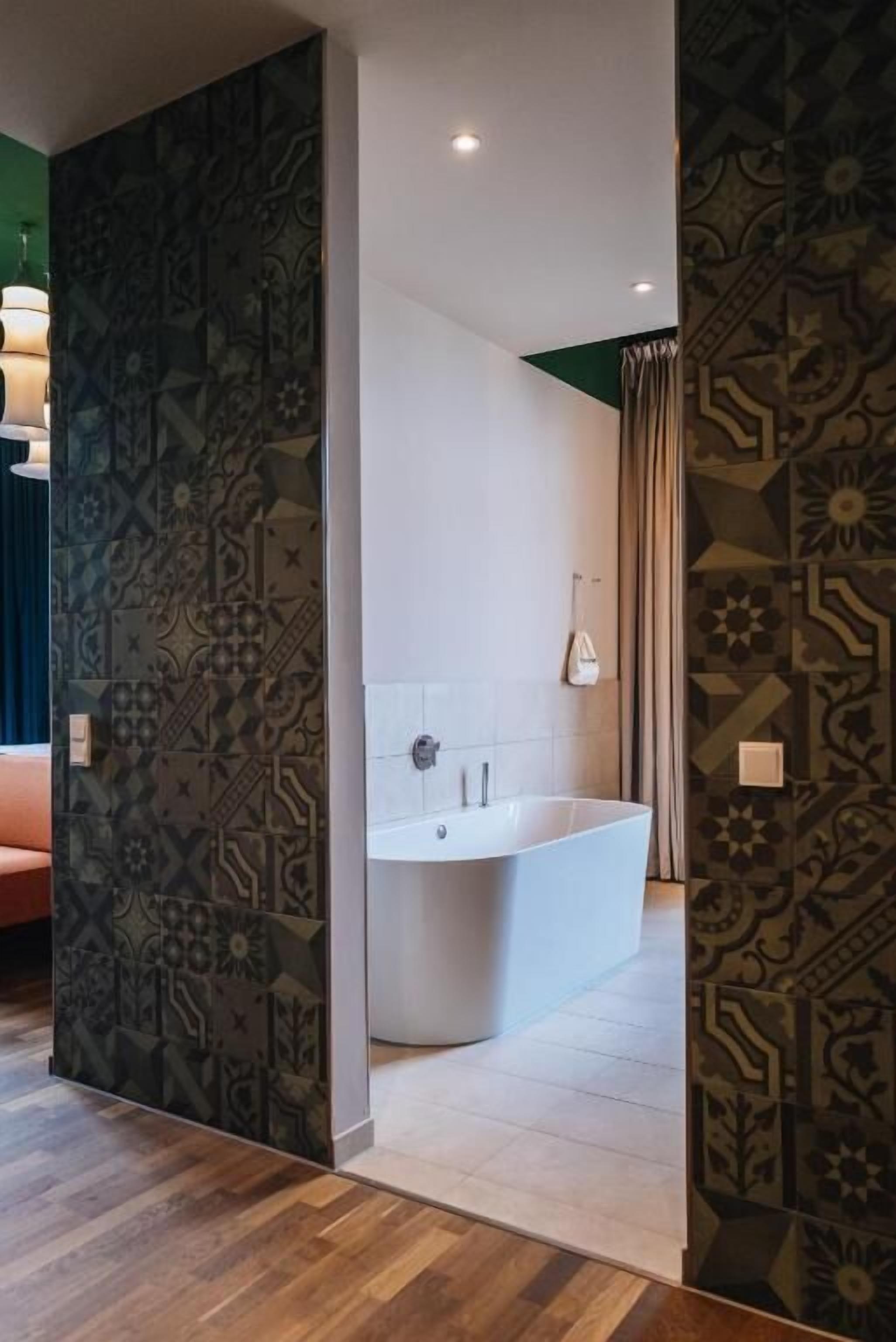 A modern bathroom with a freestanding bathtub, patterned walls, and a wooden floor.