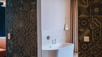 A modern bathroom with a freestanding bathtub, patterned walls, and a wooden floor.