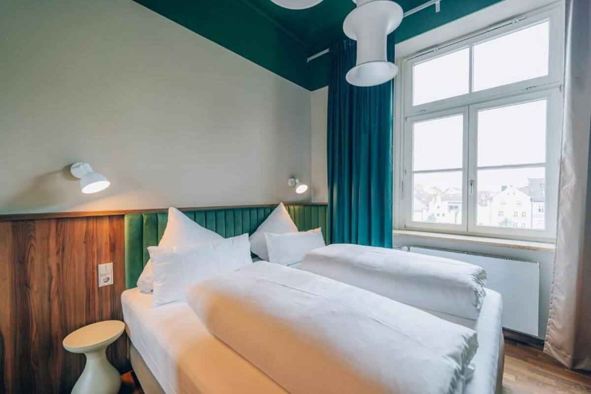 Habitación de hotel con dos camas, una pared decorativa de madera, una ventana con cortinas y vistas a edificios.