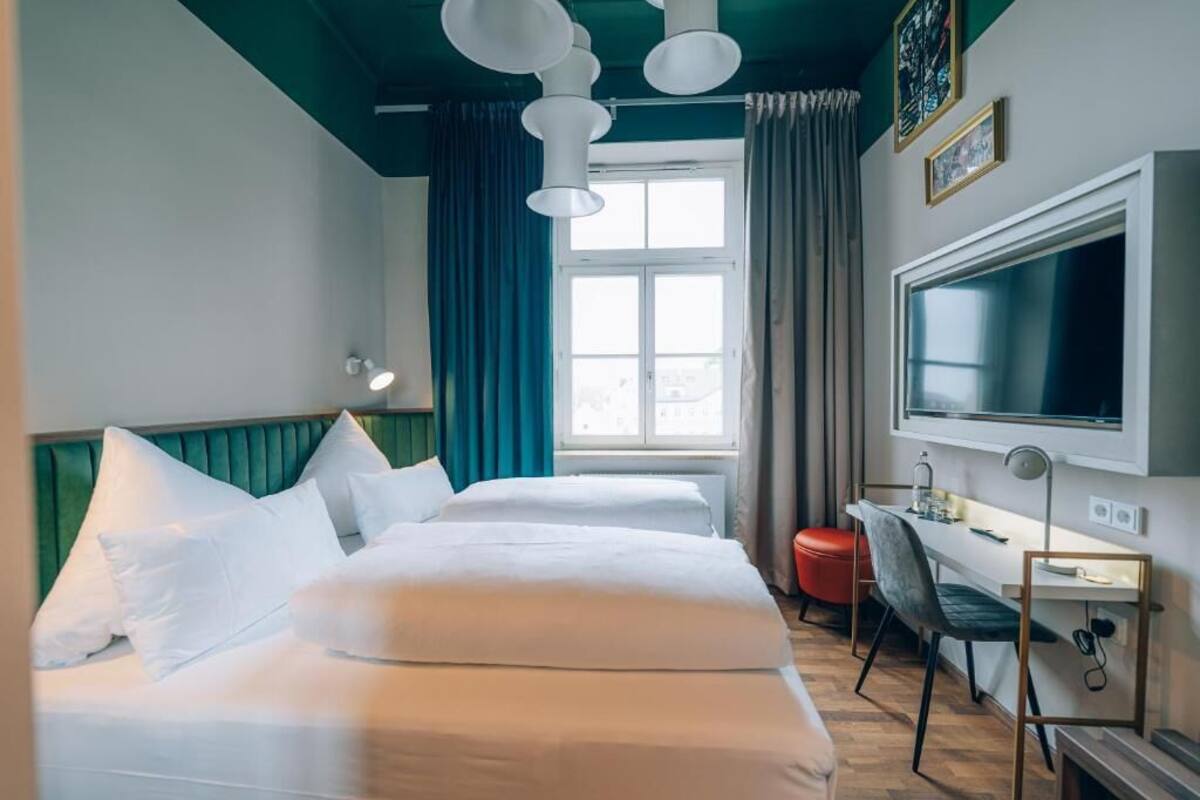Habitación de hotel con dos camas, un escritorio, una silla, un televisor y una ventana con cortinas.