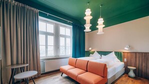 A bedroom with a bed, a sofa, a small table, and a window with curtains. - Hotel Amalia - Boutique Hotel (Landshut)
