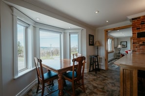 Un comedor con mesa y sillas, ventanas amplias, chimenea de ladrillo y vistas al exterior.
