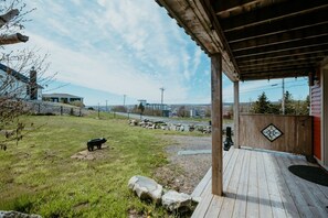 A wooden deck with a stone pathway, a stone bench, and a fenced area with a view of a cityscape.