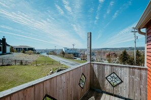 Una terraza de madera con vista a un paisaje urbano, un área con césped y una calle pavimentada.