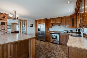 Una cocina con armarios de madera, un refrigerador, un horno y piso de baldosas de piedra.