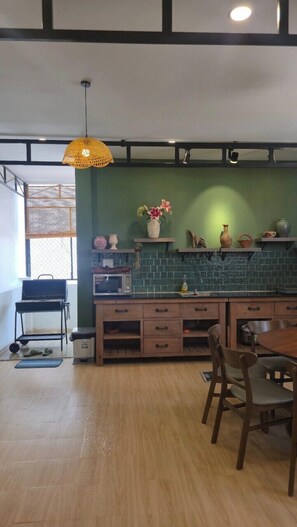 A kitchen with a green backsplash, wooden cabinets, a hanging light fixture, and a dining area with chairs. - TP HOMe (Nha Trang)