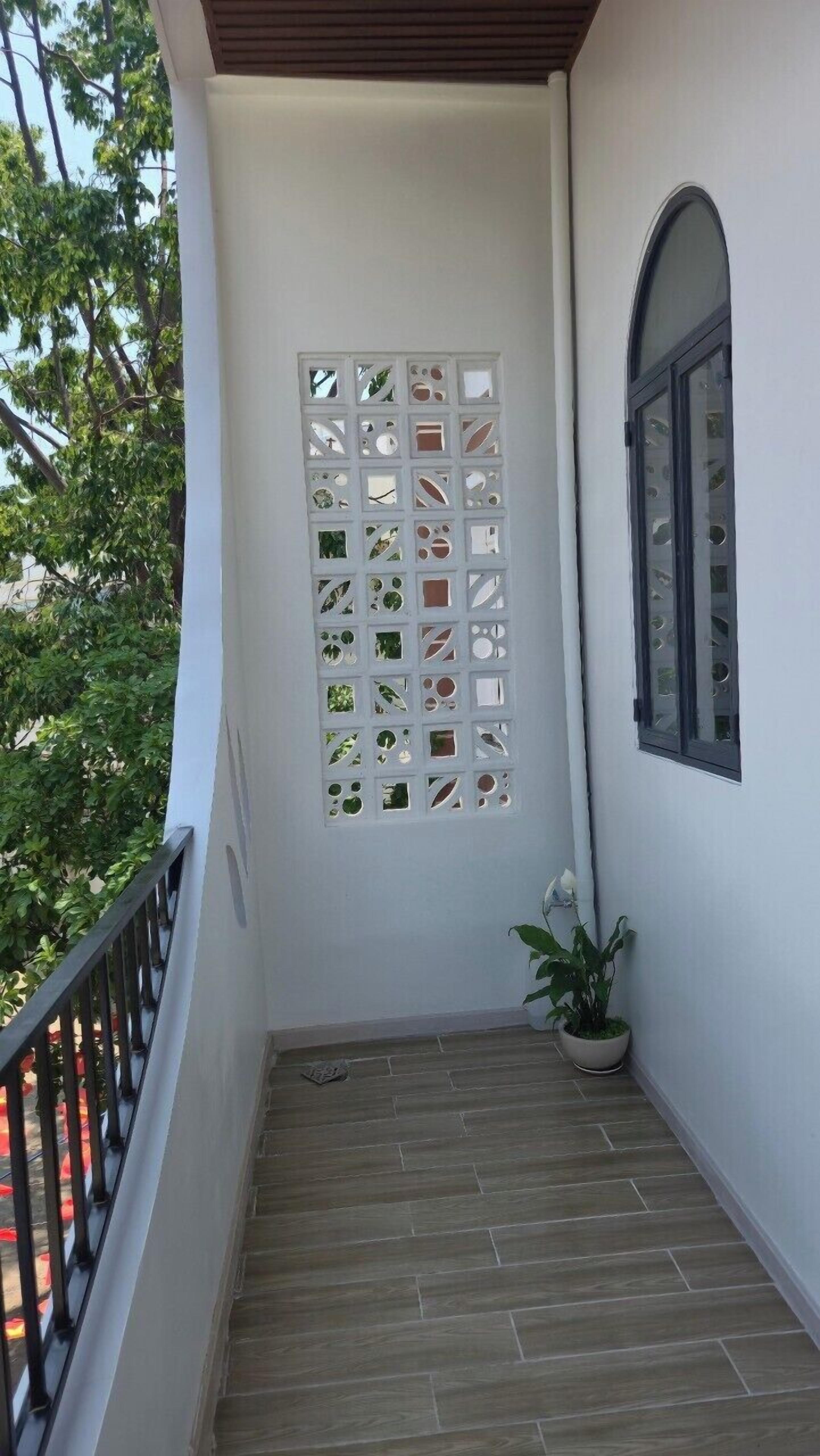 A balcony with a white wall, a decorative screen, a potted plant, and a window.