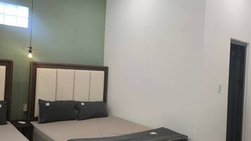 A room with two beds, a bench, an air conditioning unit, a window, and a door.