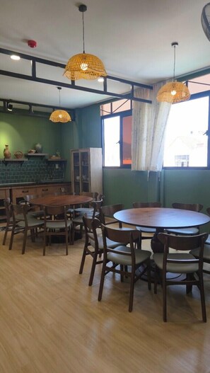 A dining area with a round table and chairs, a kitchen in the background, and a window with curtains. - TP HOMe (Nha Trang)