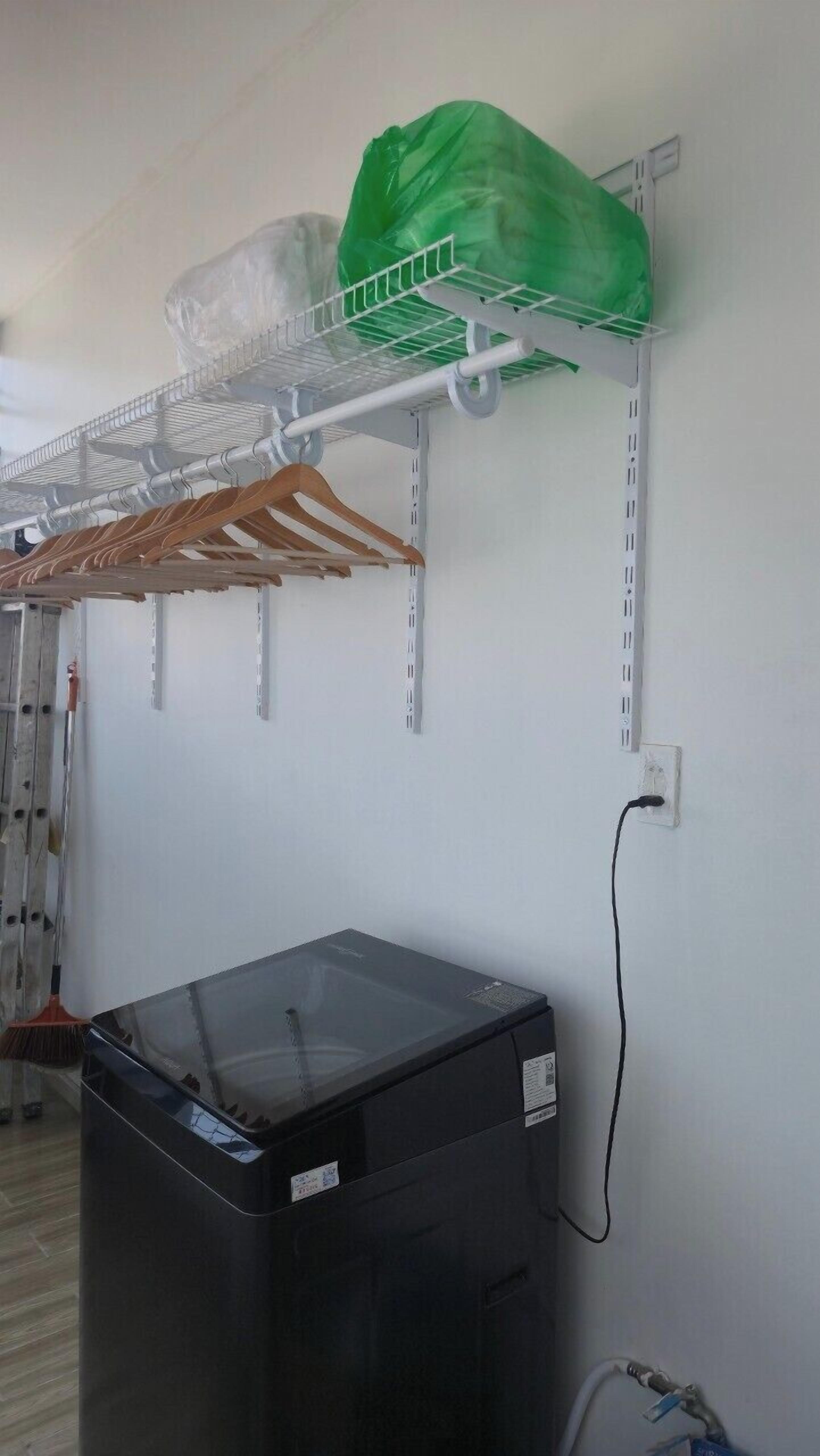 Een wasserette met een wasmachine, droogrekken en een groene plastic zak op een plank.