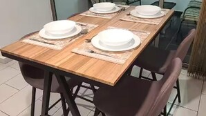 Mesa de comedor dispuesta con platos y servilletas blancas, rodeada de sillas.