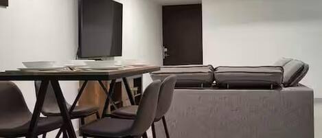 Una sala de estar moderna con un sofá, un televisor y una mesa de comedor con sillas.