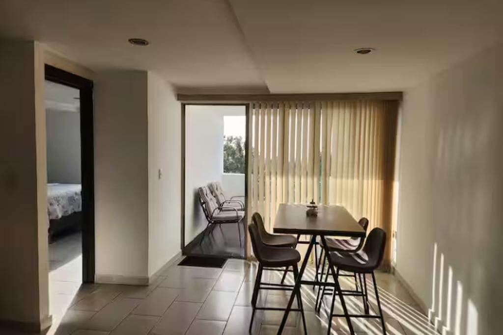 Una habitación moderna con comedor, un balcón con una silla y una cama en la habitación contigua.