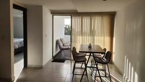 Una habitación moderna con comedor, un balcón con una silla y una cama en la habitación contigua.