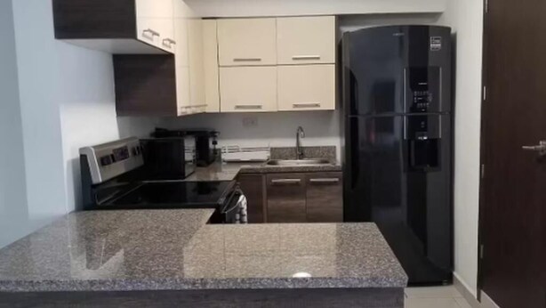 Una cocina moderna con encimeras de granito, un refrigerador negro y armarios color beige.