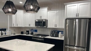Uma cozinha moderna com armários brancos, eletrodomésticos de aço inoxidável, uma ilha central e iluminação pendente.