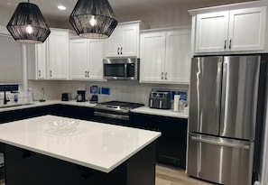 A modern kitchen with white cabinets, stainless steel appliances, a central island, and pendant lighting.
