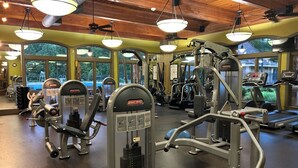 Uma academia com diversos equipamentos de exercício, janelas amplas e teto de madeira.
