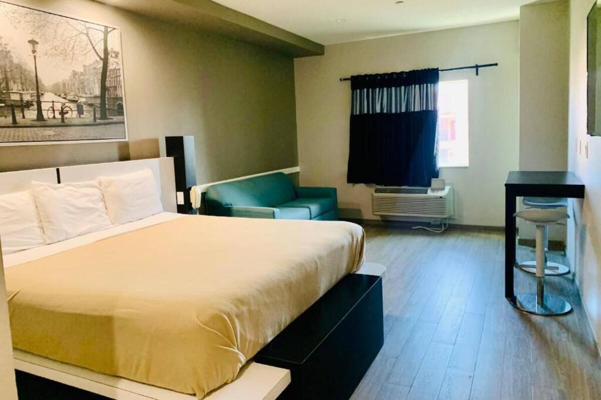 A modern hotel room with a large bed, a sofa, a desk, and a window with curtains.