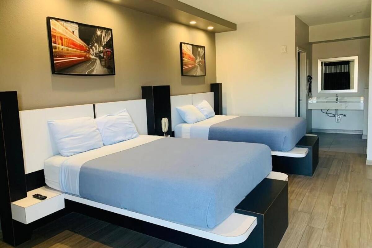 A hotel room with two beds, a bathroom with a mirror, and artwork on the walls.