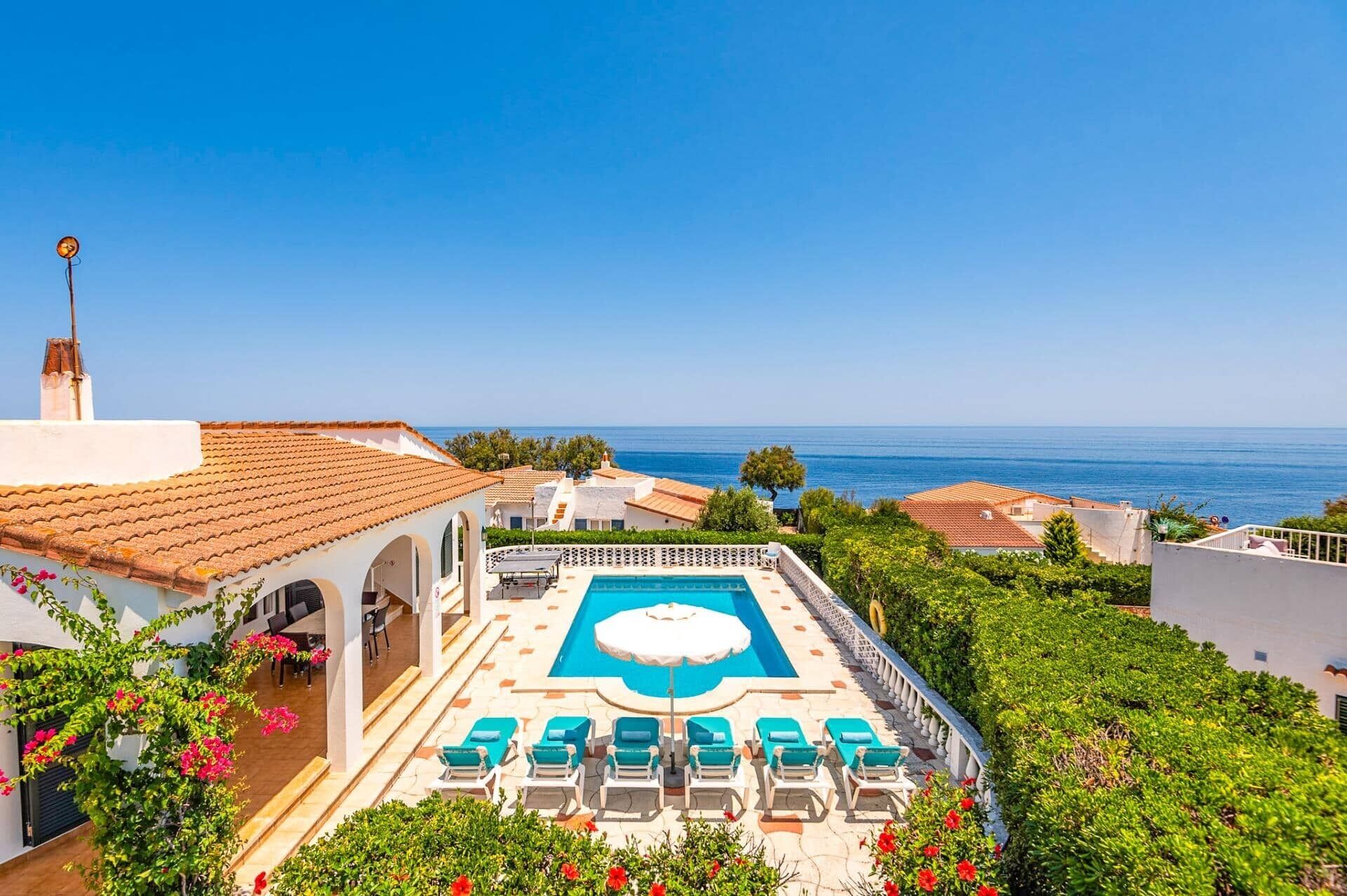 Una piscina al terrat amb gandules i una vista despejada del mar.