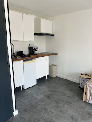 Cozinha compacta com armários brancos, coifa preta, máquina de café e uma pequena lixeira.