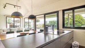 Une cuisine moderne dotée d’un grand îlot central, d’appareils électroménagers intégrés et de grandes fenêtres offrant une vue sur l’extérieur.