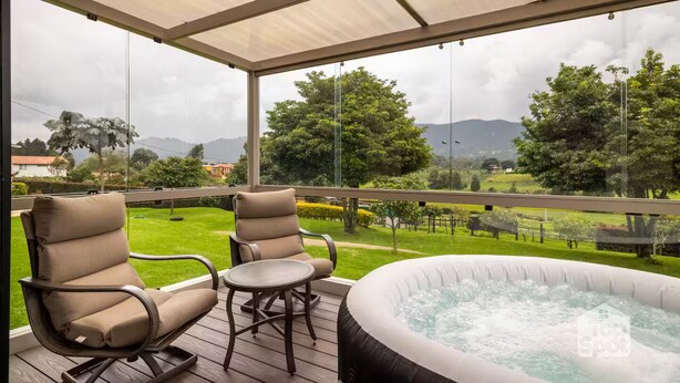 Un espace extérieur abrité, doté de deux chaises et d’un jacuzzi, qui offre une vue sur un paysage verdoyant, avec des arbres et des montagnes.