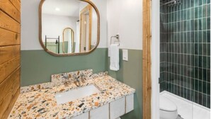 Une salle de bain avec un mur en bois, un lavabo doté d’un plan de travail à motifs, un miroir et une douche aux carreaux verts.