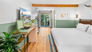 Une chambre à coucher avec un lit, un bureau et une vue sur l’extérieur, visible à travers une porte vitrée.