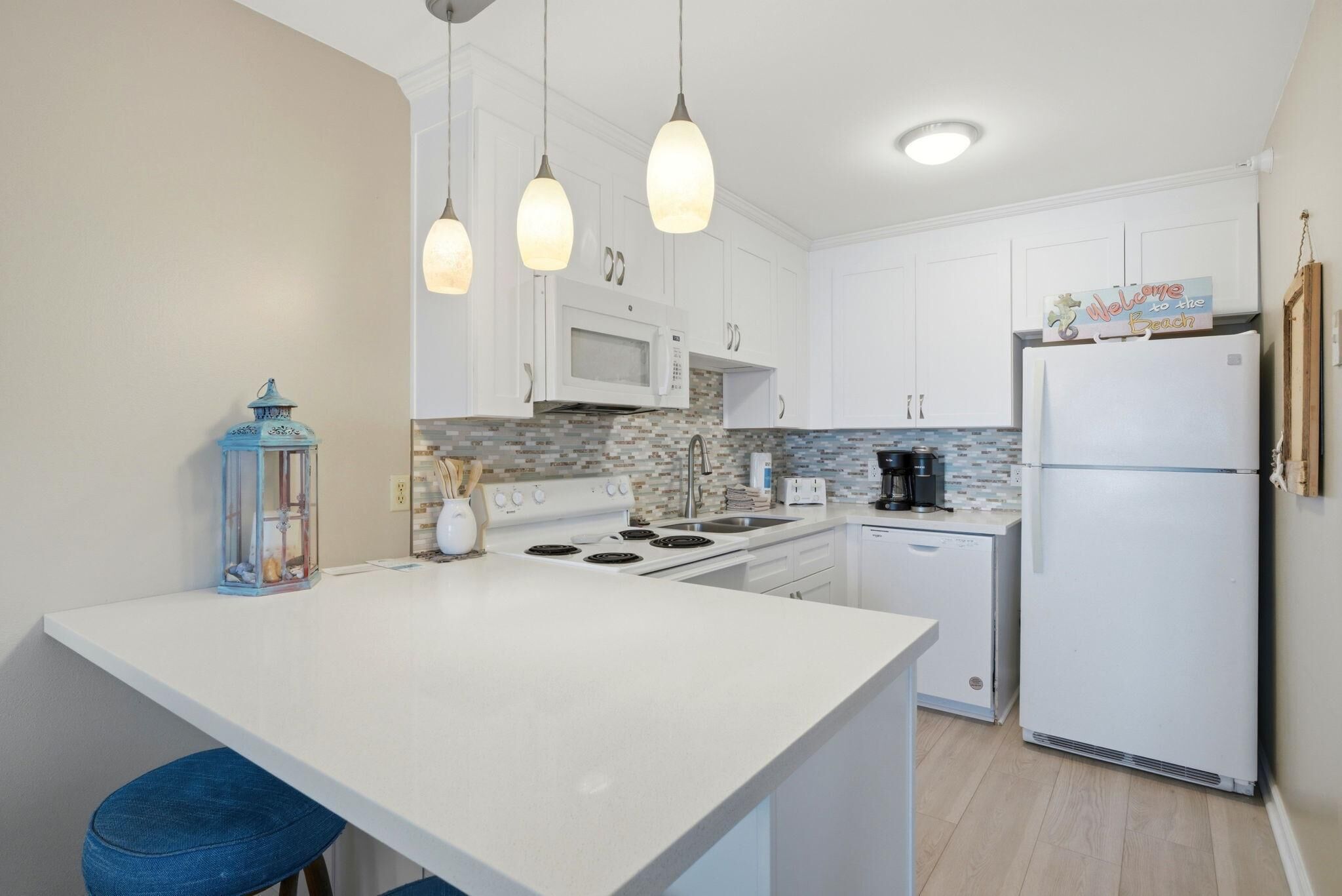 A modern kitchen with white cabinets, a central island, a microwave, stove, and a refrigerator.