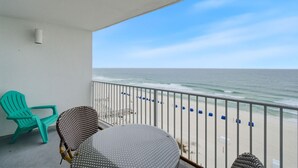 Een balkon met uitzicht op de oceaan, een groene stoel, een gestreept stoel en een klein tafeltje.