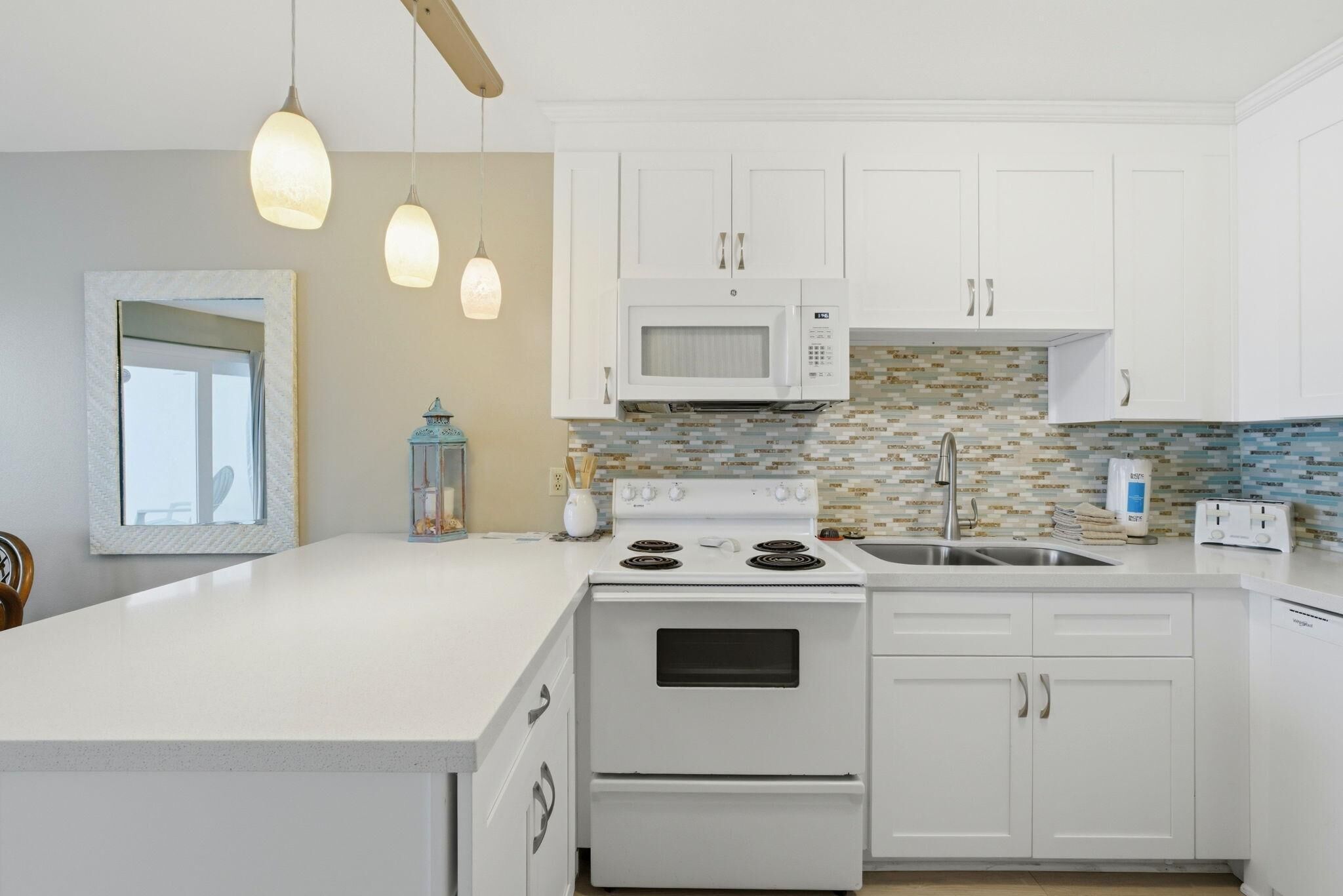 A modern kitchen with white cabinetry, a microwave, stove, and a tiled backsplash.