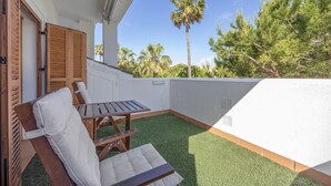 A balcony with a wooden table and chairs, a palm tree, and a view of other trees. - Levante Sancti Petri Apartment with Shared Pool, Wi-Fi, and Air Conditioning (Chiclana de la Frontera)
