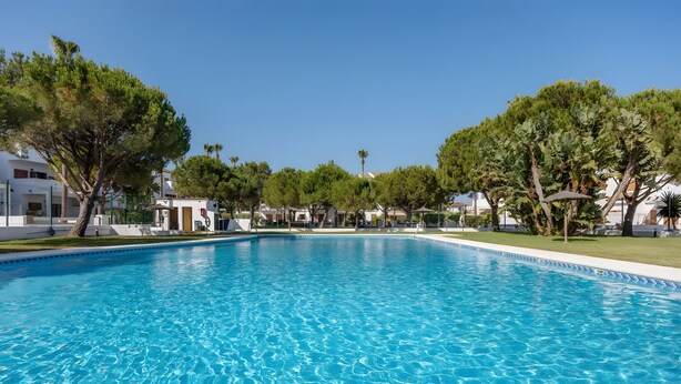 A clear blue swimming pool surrounded by trees and white buildings. - Levante Sancti Petri Apartment with Shared Pool, Wi-Fi, and Air Conditioning (Chiclana de la Frontera)