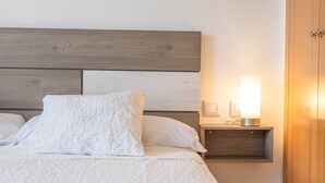 A neatly made bed with a wooden headboard, a bedside table with a lamp, and a wooden wardrobe. - Levante Sancti Petri Apartment with Shared Pool, Wi-Fi, and Air Conditioning (Chiclana de la Frontera)
