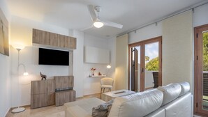 A modern living room with a flat-screen TV, a ceiling fan, a sofa, and a dining area. - Levante Sancti Petri Apartment with Shared Pool, Wi-Fi, and Air Conditioning (Chiclana de la Frontera)