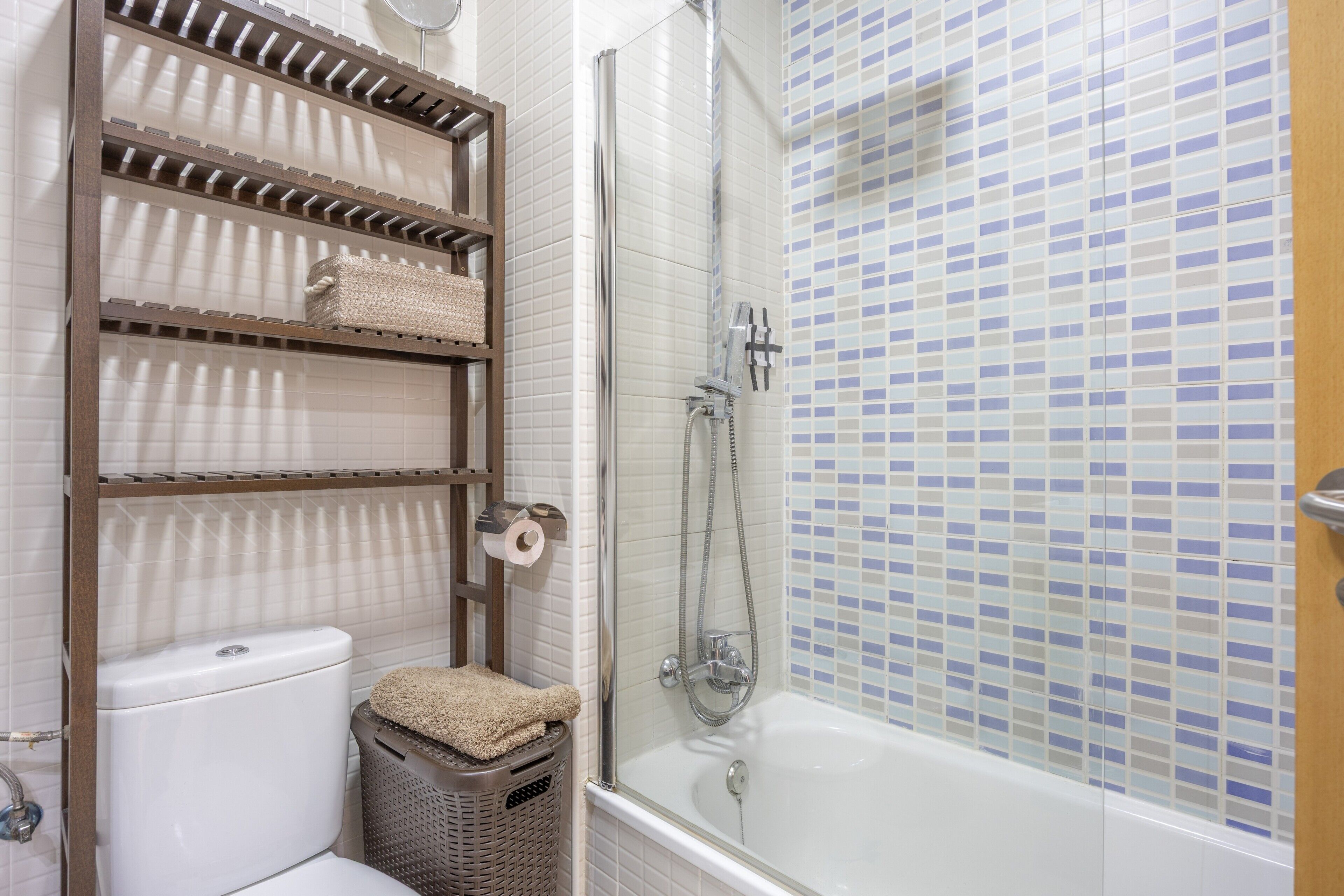 A bathroom with a toilet, a shower, a sink, and a shelf with towels.