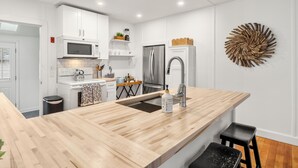 Una cocina moderna con armarios blancos, una isla de madera con un lavamanos y un elemento decorativo en la pared.