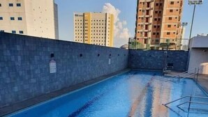 Une piscine avec des lignes de démarcation bien visibles dans chaque couloir, entourée d’un mur de pierre, et des immeubles de grande hauteur en arrière-plan.