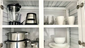 Una cocina con licuadora, cafetera, ollas y platos blancos apilados.
