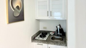 Una cocina compacta con gabinetes blancos, encimera de granito, estufa a gas y un lavamanos.